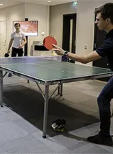 Two students playing table tennis with an information screen in the background
