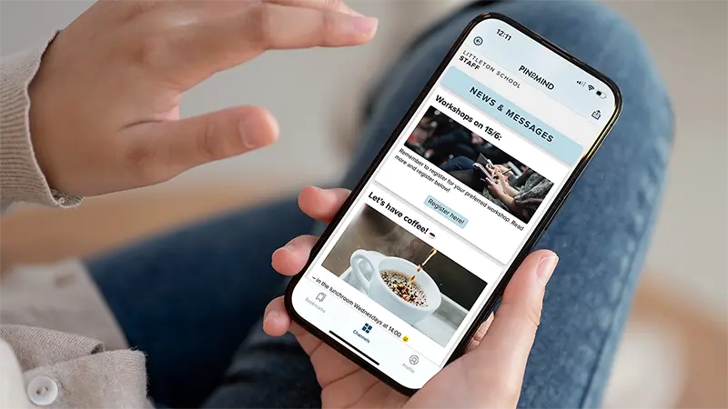 A person holding a mobile phone with PinToMind Go open, showing a channel with information for school staff, including messages and updates relevant to their workday. Photo