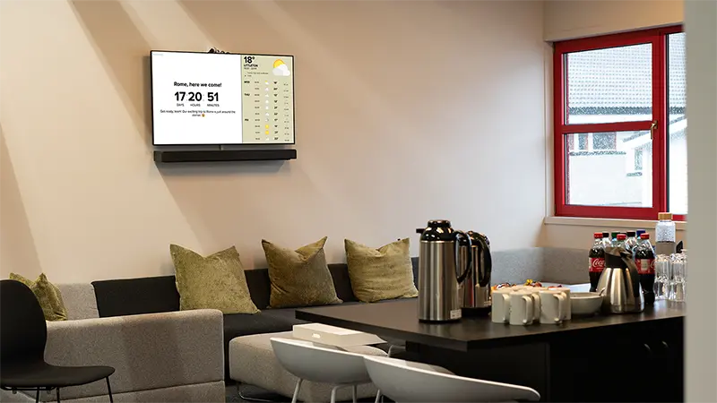 An information screen in a lounge area shows a countdown to a trip to Rome and weather forecasts. Photo.