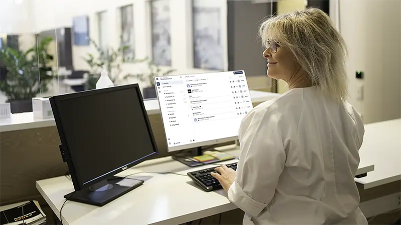 The photo shows a woman at work in a hospital managing PinToMind from her PC.